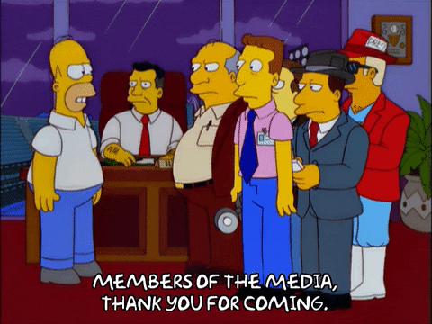 Homer Simpson stands in front of a group of men, including reporters and officials, in an office. Text reads, MEMBERS OF THE MEDIA, THANK YOU FOR COMING—hoping to attract media attention like a promising start-up.