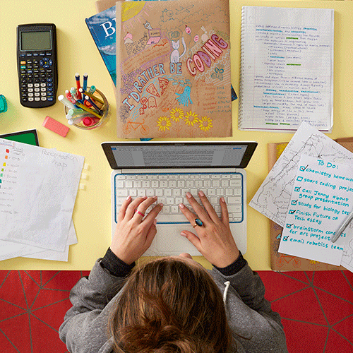 A person types on a laptop at a cluttered desk with notebooks, colourful pens, a calculator, and a to-do list—papers scattered about include doodles and “I’d Rather Be Coding,” capturing the creative chaos of start-up life.