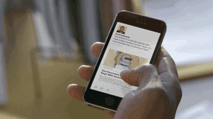 A person scrolls through an article on a mobile phone using their thumb. The article, discussing how start-ups can attract media attention, features an image of a cartoon robot and text beneath a profile photo at the top.