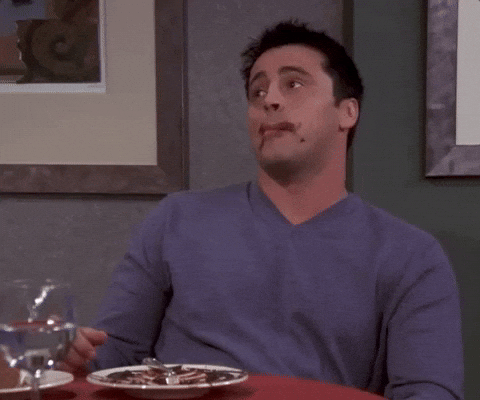 A man in a purple jumper sits at a table in a restaurant, looking around and awkwardly licking his lips with a bit of food on his mouth—an unexpected moment perfect for creating shareable social media content.