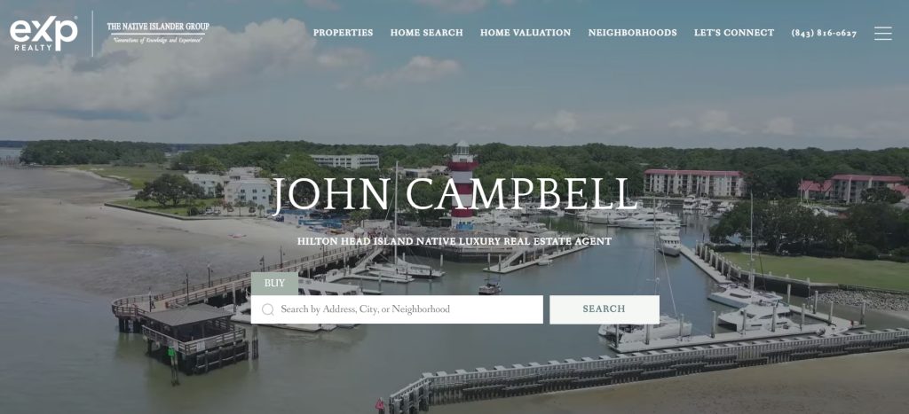 A waterfront marina with jetties, boats, and a red-and-white lighthouse, set against buildings and trees. The website highlights Hilton Head Island estate agent John Campbell and features a central search bar for higher conversions.